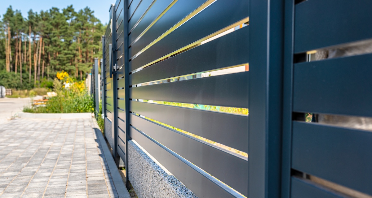 Modern panel fencing in anthracite color, visible spans and a wicket, forest in the background.